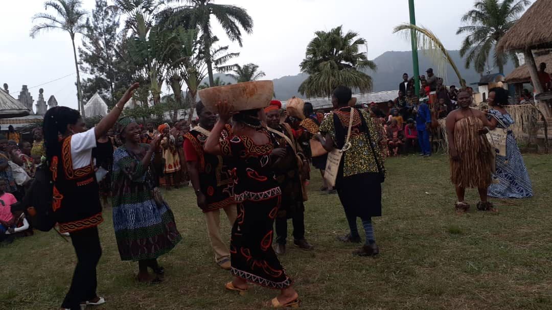 Dancers in Meta dress on the palace ground, one carrying a carved wooden bowl on her head
